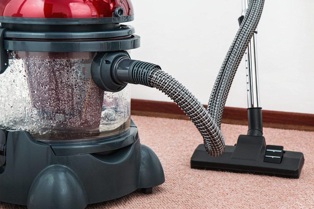 Close-up of a red vacuum cleaner with a flexible hose, positioned on a carpeted floor, showcasing its design and functionality for effective cleaning.