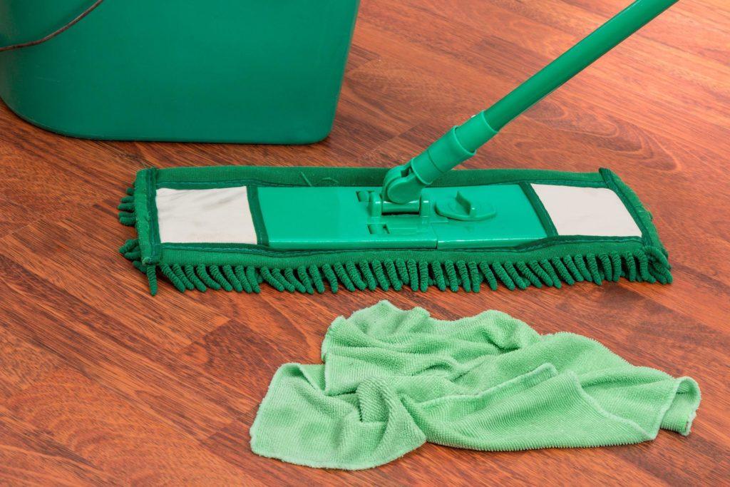 Green cleaning mop on hardwood floor with a microfiber cloth nearby for efficient dusting and cleaning.