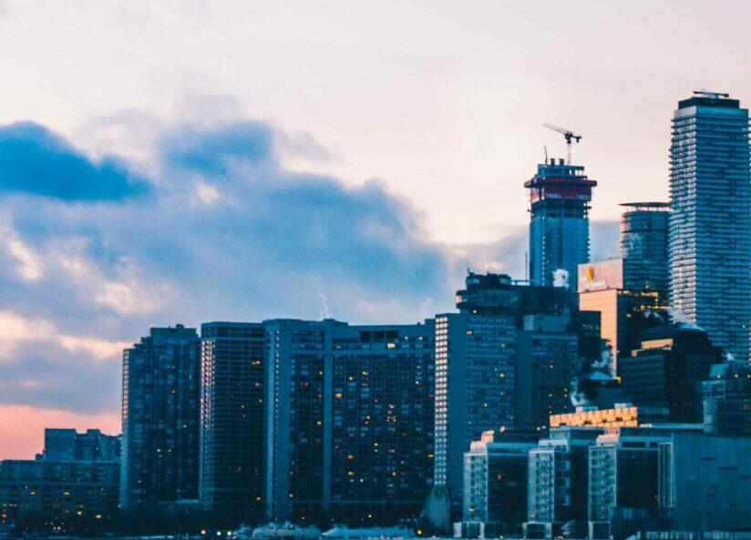 City skyline at dusk featuring modern skyscrapers and a construction crane against a backdrop of cloudy skies.