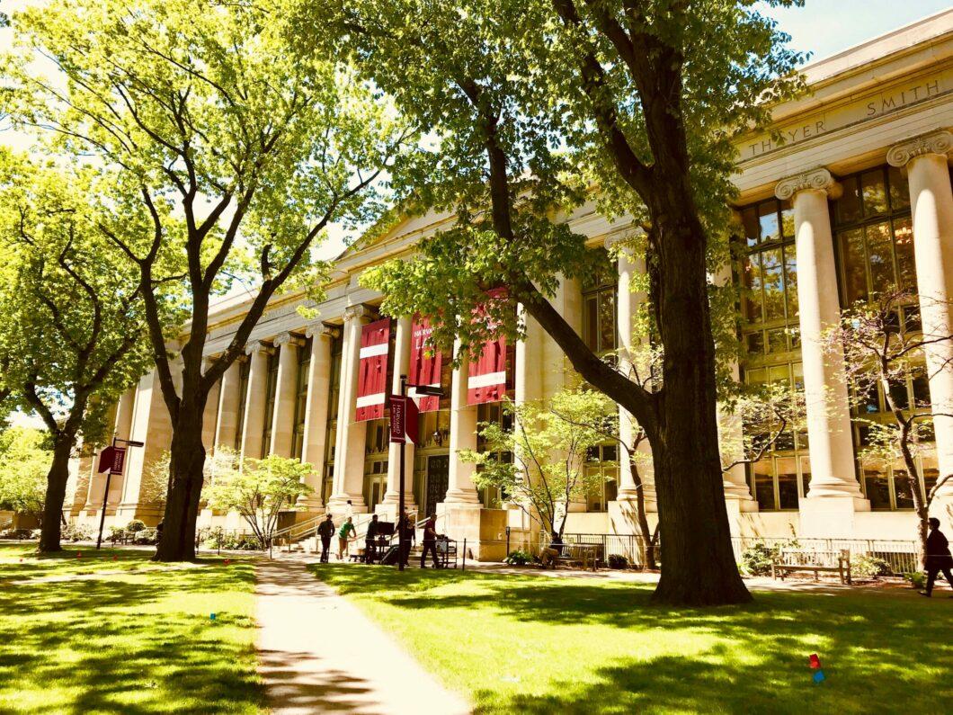 Harvard University library building surrounded by lush green trees and a well-maintained lawn, showcasing its classic architecture and vibrant campus life.