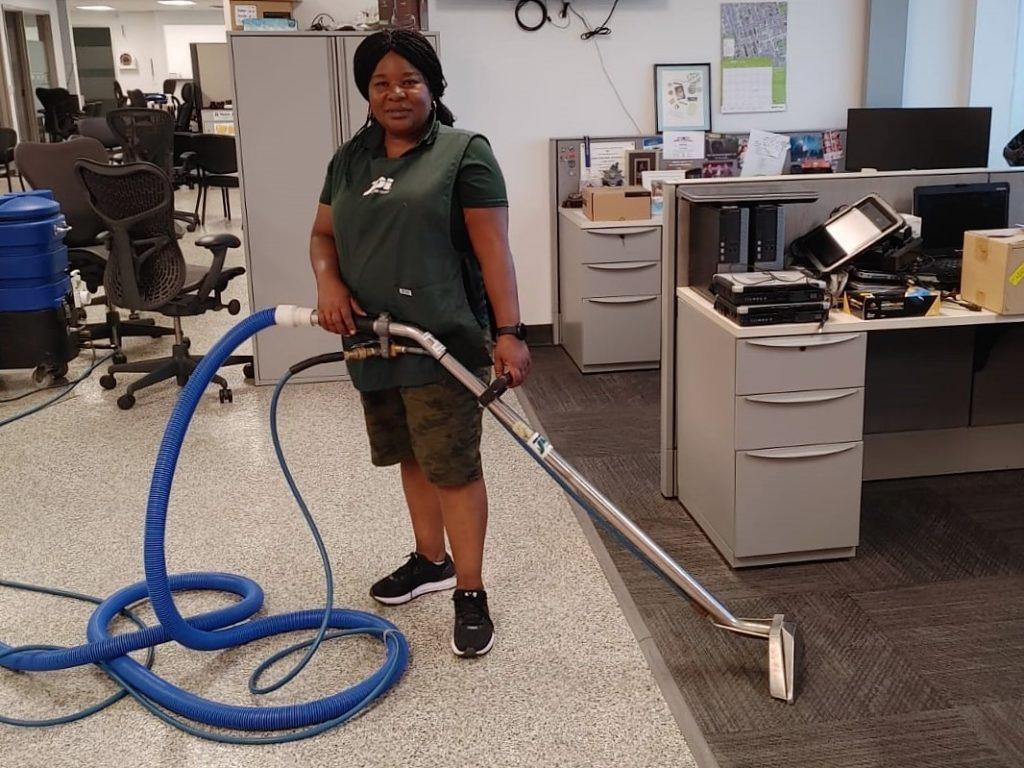Woman using a carpet cleaning machine in an office environment, showcasing professional cleaning services.