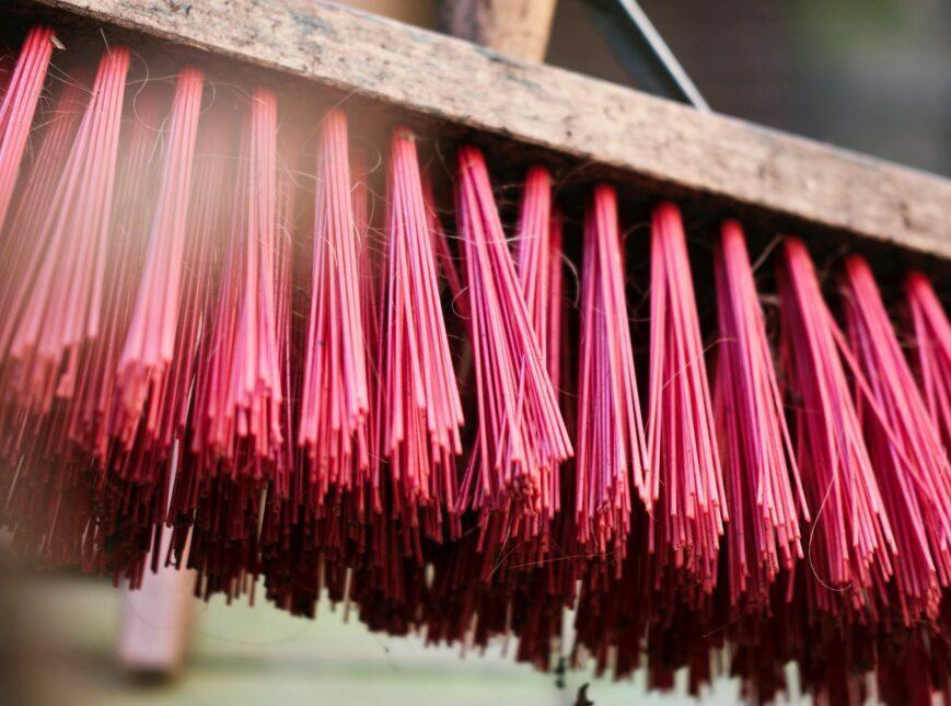 Close-up of vibrant red incense sticks hanging in a row, showcasing their fine texture and color. The image captures the intricate details of the sticks, highlighting their use in traditional rituals and ceremonies.