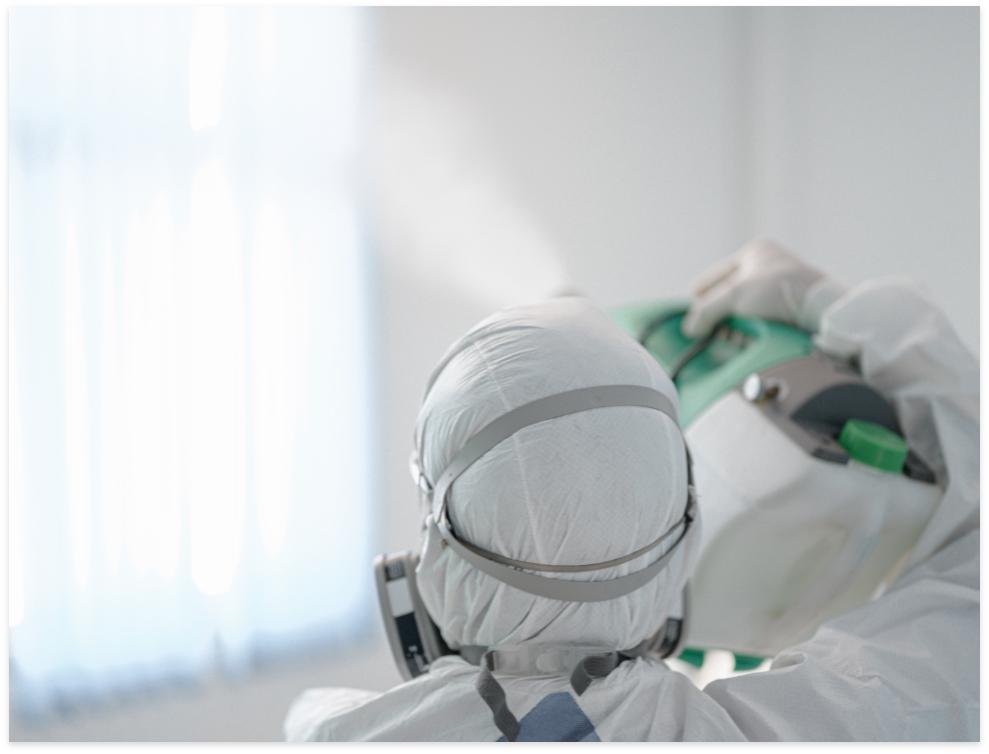 Medical professional in protective gear applying disinfectant in a clean environment.